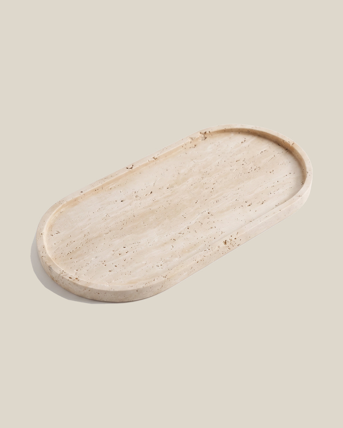 ATOMS OVAL Tray in beige travertine, angled view on a BONE background