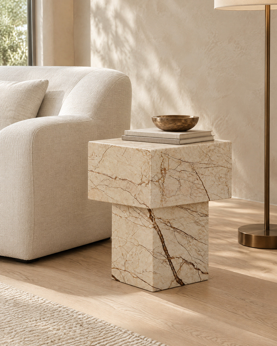 BUTTER side table by CARVINGS in Sofita Beige Marble, in a styled living room, left view.